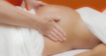 Pregnant young latina woman with beautiful skin, being wrapped with a towel, lying on a bed and having a relaxing prenatal massage, various techniques, glamour clarity effect