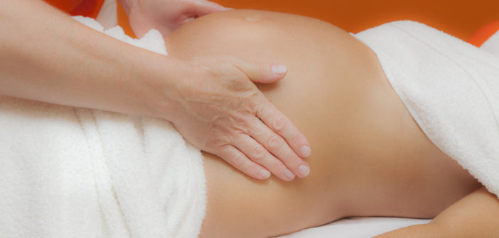 4 Reasons to Receive a Prenatal Massage Pregnant young latina woman with beautiful skin, being wrapped with a towel, lying on a bed and having a relaxing prenatal massage, various techniques, glamour clarity effect
